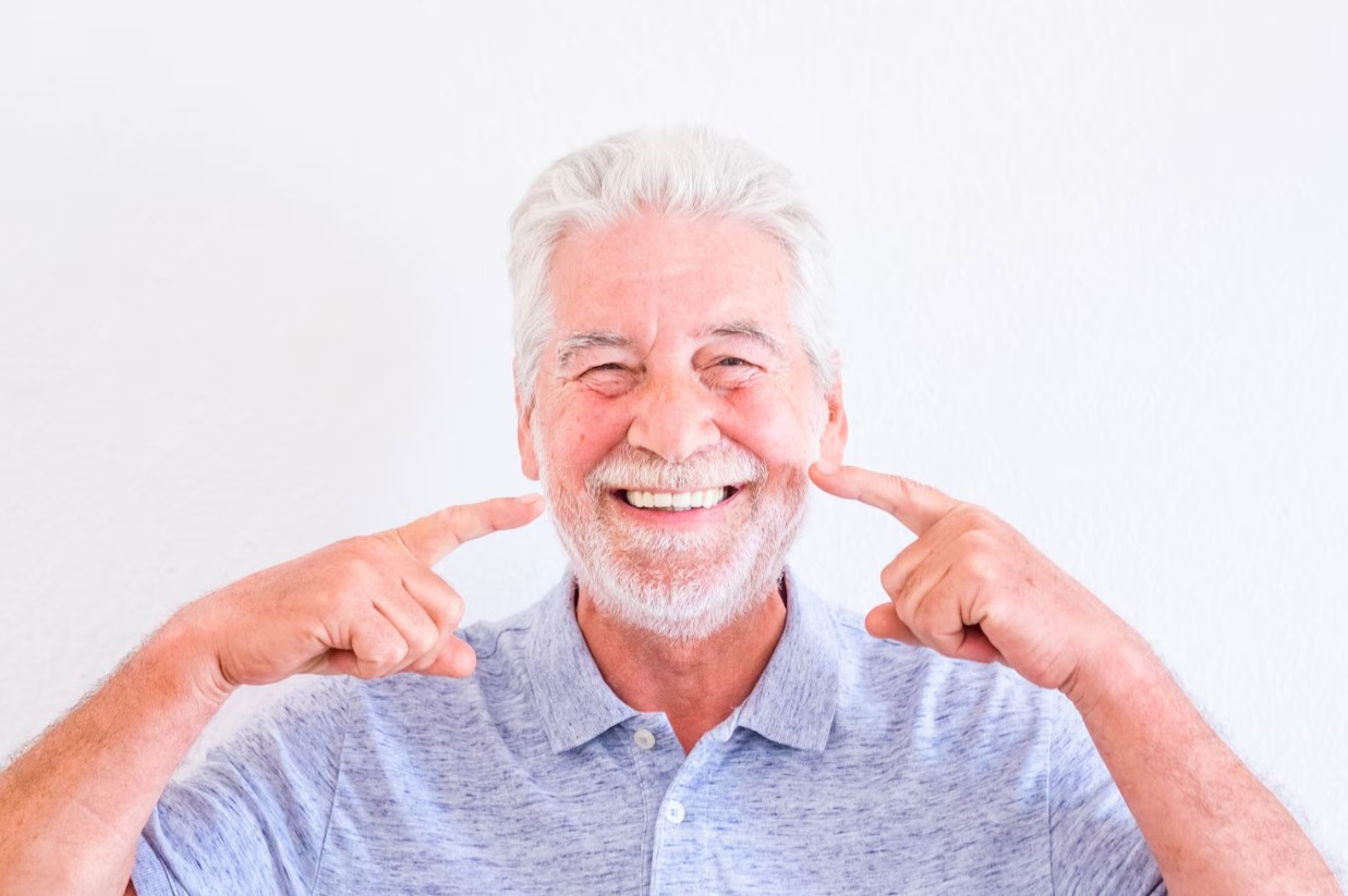 Smiling older man pointing at his teeth, showcasing dental health, relevant to Invisalign treatment options at Laguna Niguel Dental.